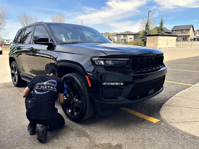 An O Detail team member cleaning the wheel on a black Jeep Grand Cherokee